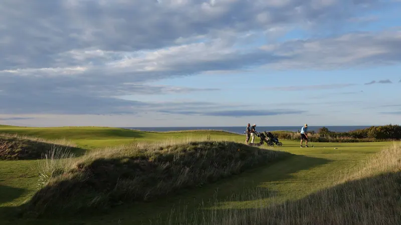 Golfers walking a dune-lined fairway in evening light
