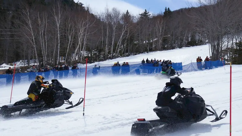 Snowmobiles racing on a snowy course with spectators