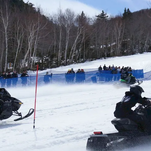 Snowmobiles racing on a snowy course with spectators