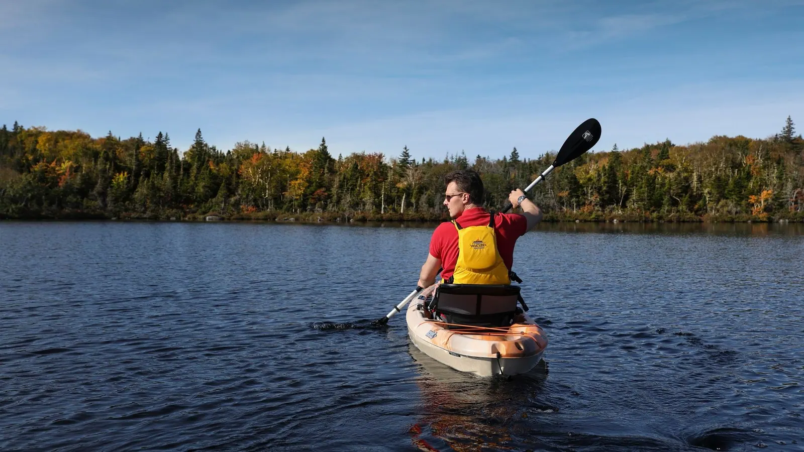 Canoe gliding across calm water below forested hills