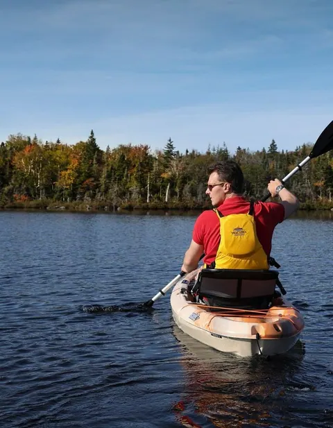 Canoe gliding across calm water below forested hills