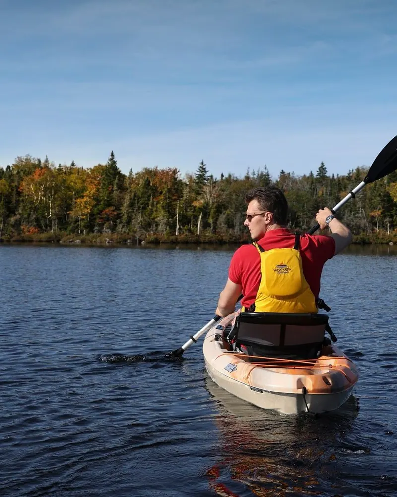 Canoe gliding across calm water below forested hills