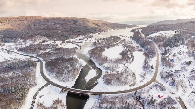 Aerial view of the Cabot Trail curving across a bridge through a snowy river valley