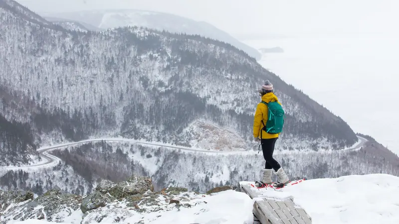 Snowshoer in a yellow jacket looking over a snowy valley