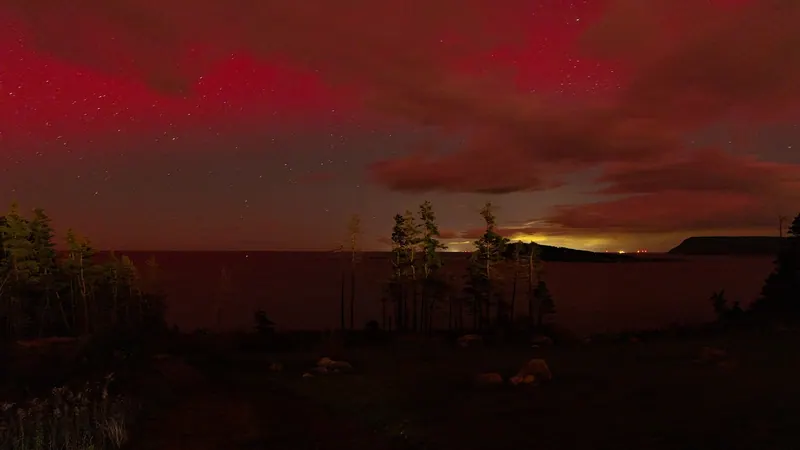 Deep red aurora glowing above a dark shoreline at night