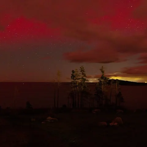 Deep red aurora glowing above a dark shoreline at night