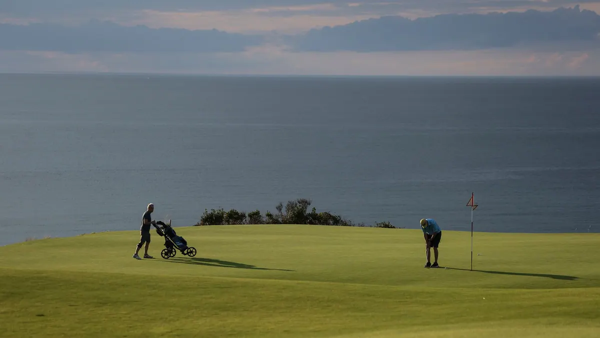 Golfers on a green above the ocean