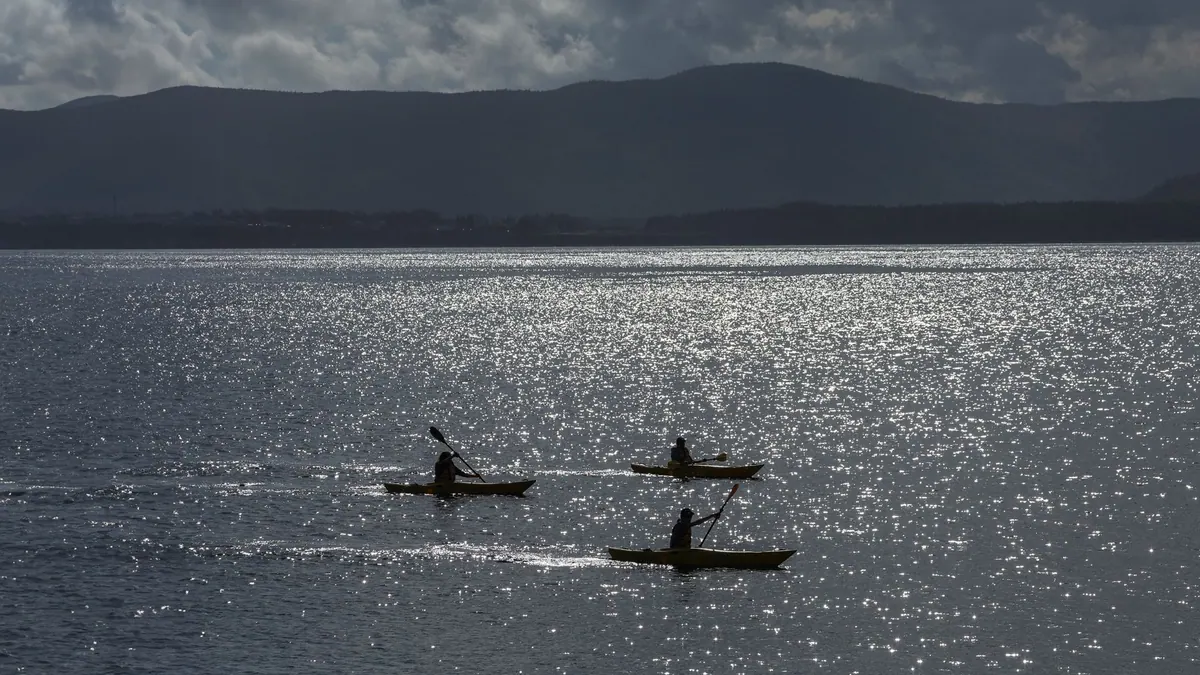 Three kayakers paddling across sparkling water