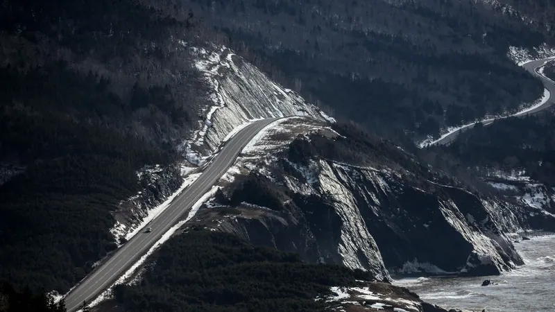The Cabot Trail climbing a dark, snow-streaked mountainside above the sea