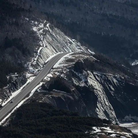 The Cabot Trail climbing a dark, snow-streaked mountainside above the sea