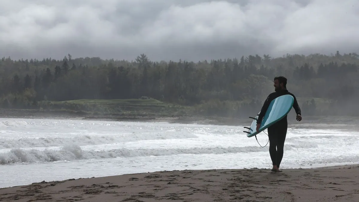 Surfer in a wetsuit walking into the waves with a board