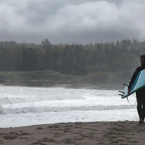 Surfer in a wetsuit walking into the waves with a board