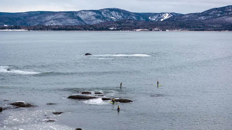 Paddleboarders on a wide calm bay below snowy hills