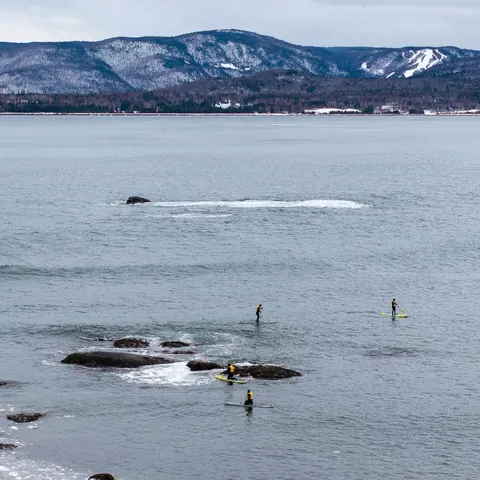Paddleboarders on a wide calm bay below snowy hills