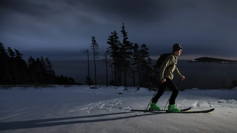 Snowshoer with a headlamp at dusk among snowy spruce