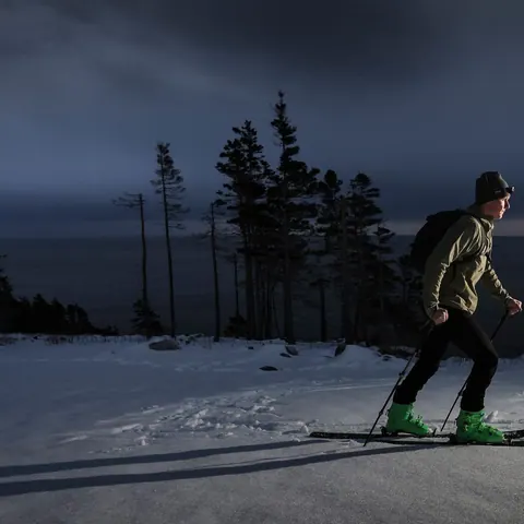 Snowshoer with a headlamp at dusk among snowy spruce