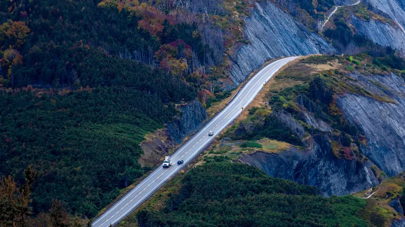 Cars on the Cabot Trail winding along a forested cliff