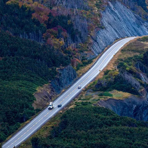 Cars on the Cabot Trail winding along a forested cliff