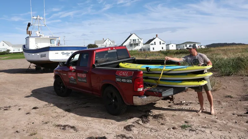 Surfboards being loaded onto a red pickup truck by the beach