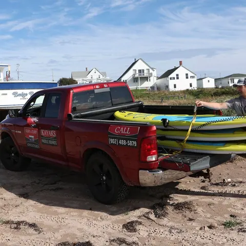 Surfboards being loaded onto a red pickup truck by the beach