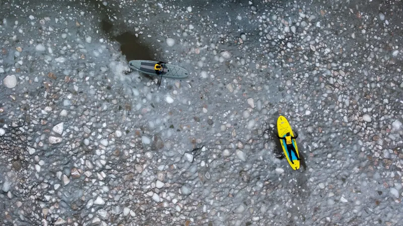 Aerial view of a yellow paddleboard over clear water and pebbles