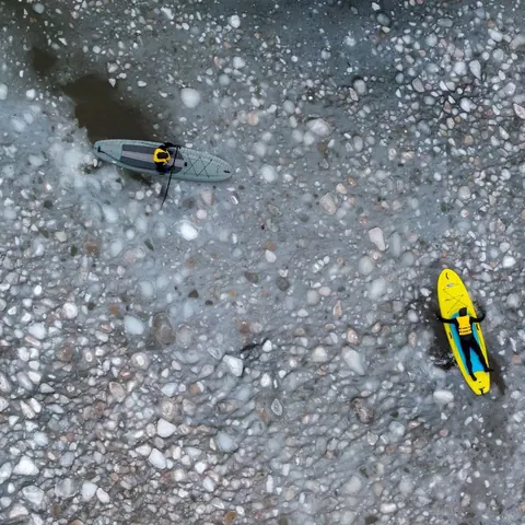Aerial view of a yellow paddleboard over clear water and pebbles