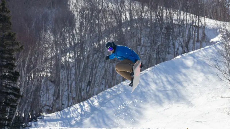 Snowboarder riding a snowy bank below bare trees