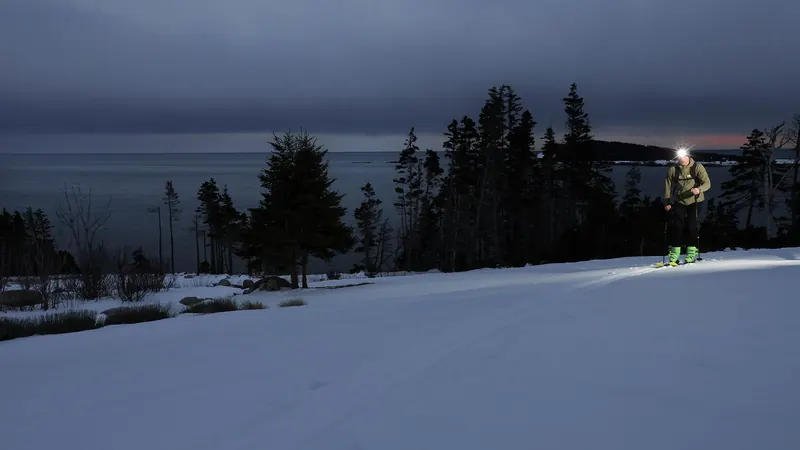Snowshoers with headlamps on a snowy shore at twilight