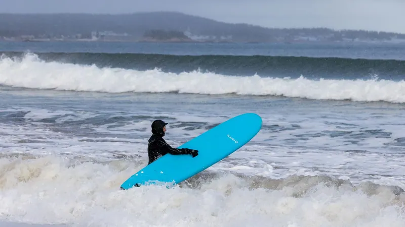 Surfer carrying a blue board through the whitewater