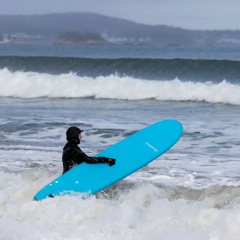 Surfer carrying a blue board through the whitewater