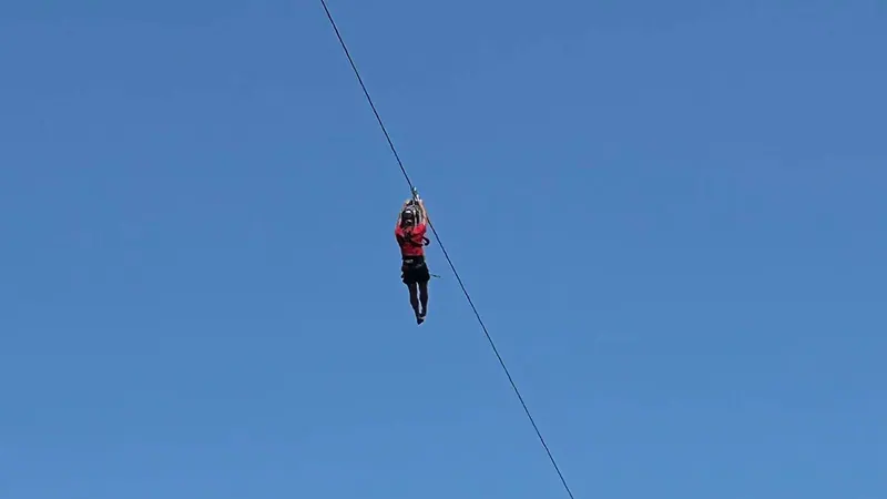 Zipline rider gliding against a blue sky