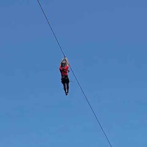 Zipline rider gliding against a blue sky