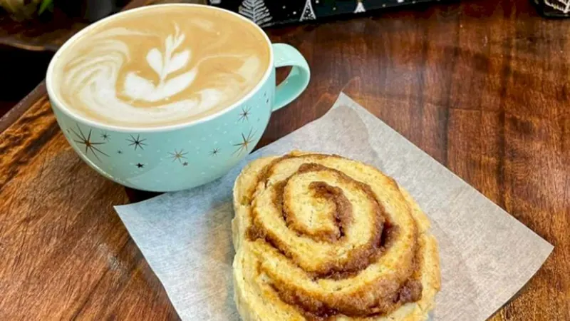 Latte with leaf art next to a cinnamon bun