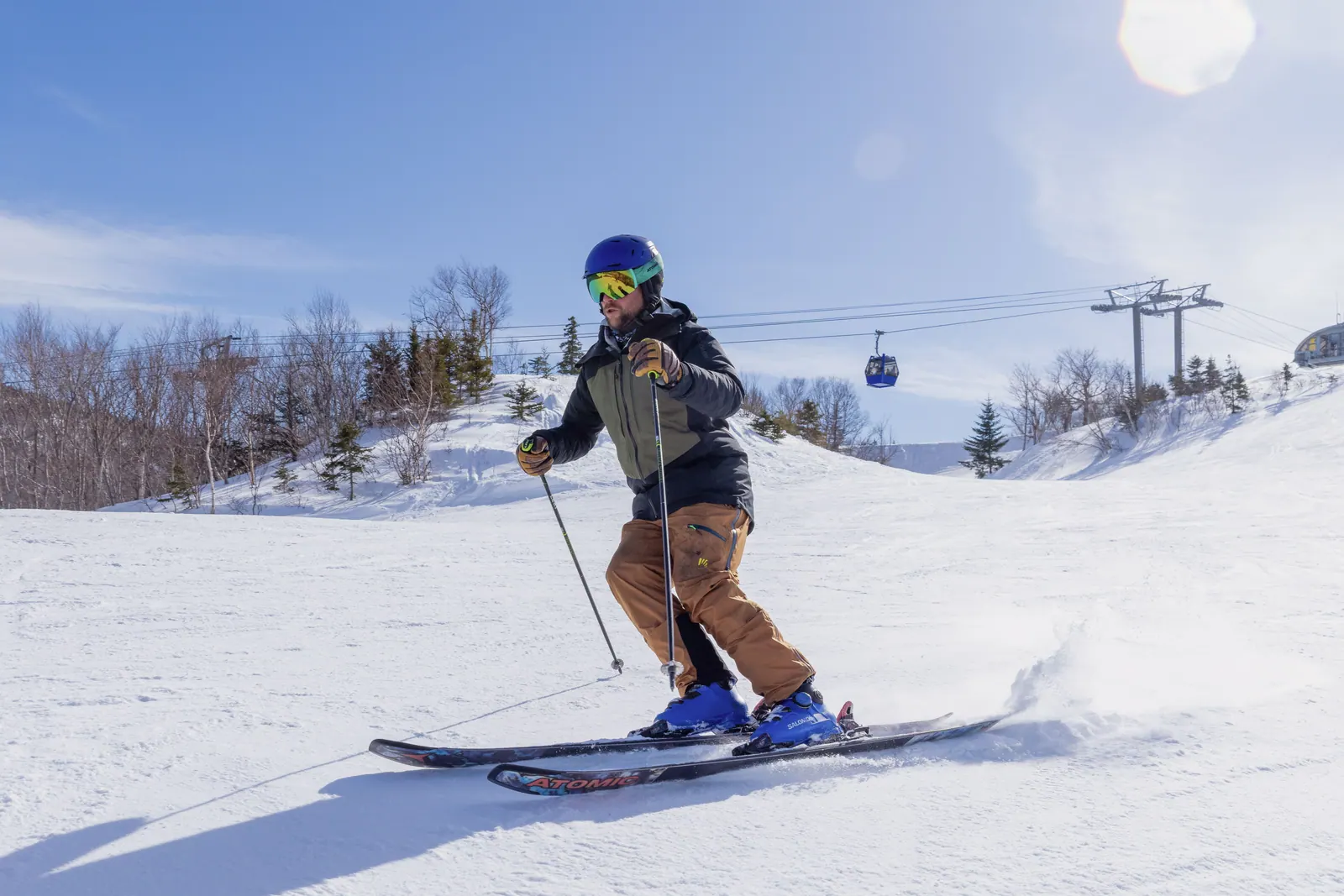 Skier on a groomed run at Cape Smokey with the gondola and the frozen coast behind