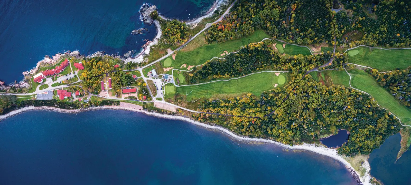 Aerial view of a golf course on a forested peninsula between deep blue Atlantic bays