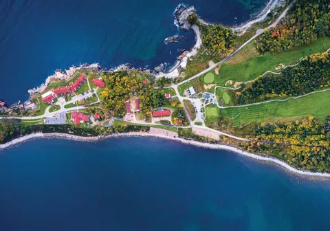 Aerial view of a golf course on a forested peninsula between deep blue Atlantic bays
