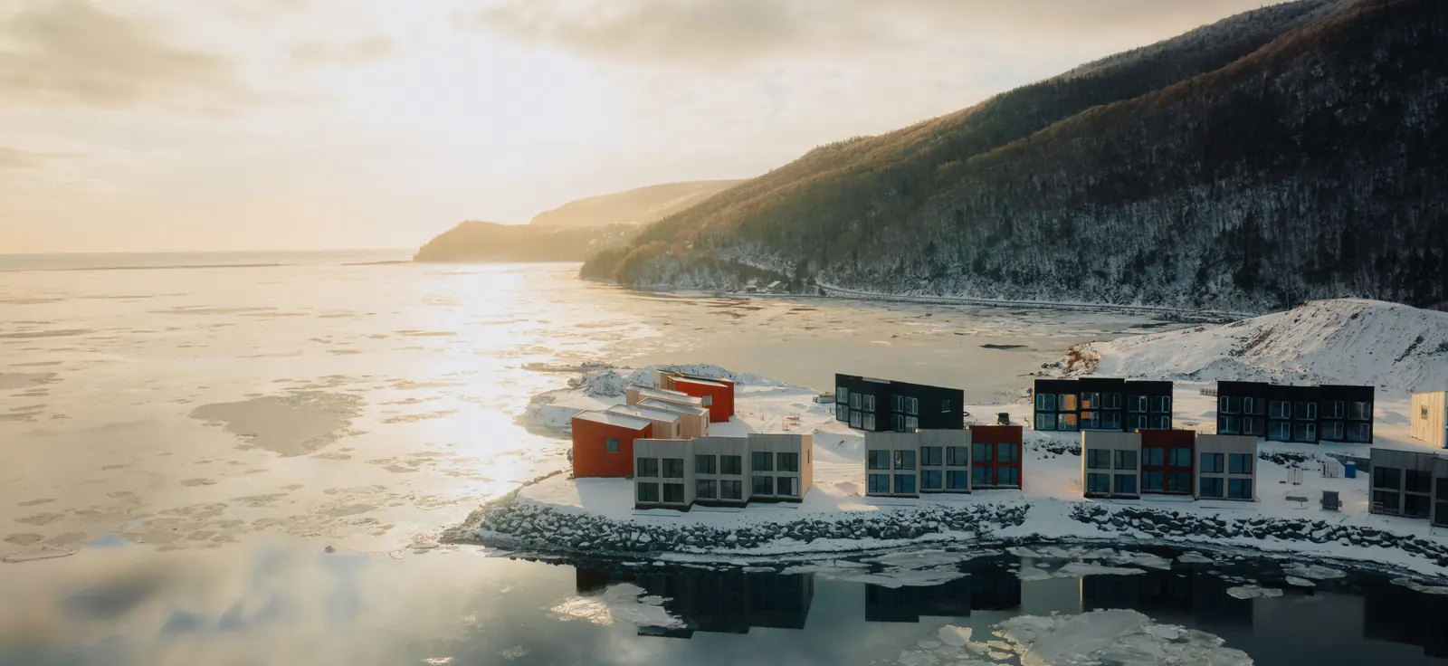 Cormorant Rock chalets on the rocky Atlantic shore in winter, with Cape Smokey rising across the bay