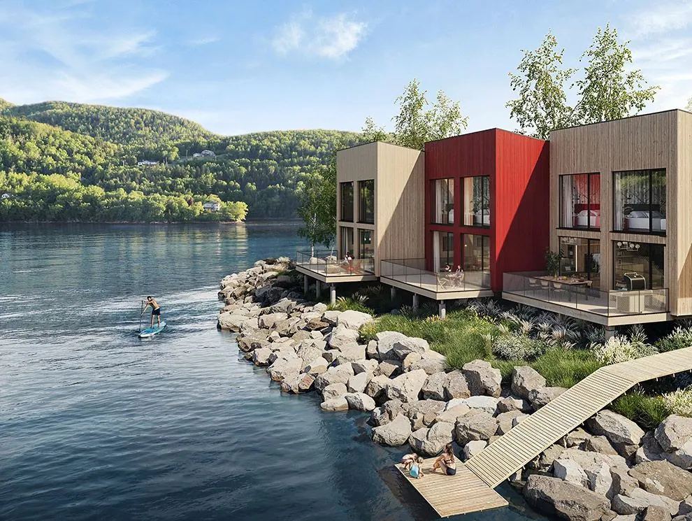 Modern timber and red chalets on a rocky point by the water, with a paddleboarder and forested hills behind
