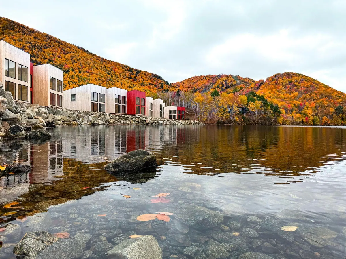 Chalets reflected in clear water below hills in full autumn colour