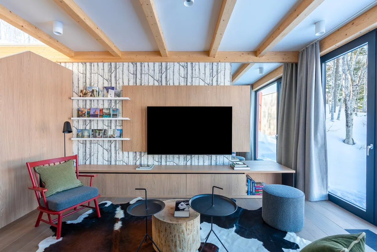 Chalet living room with a red armchair, birch-tree wallpaper, wall-mounted TV and a window onto snowy woods
