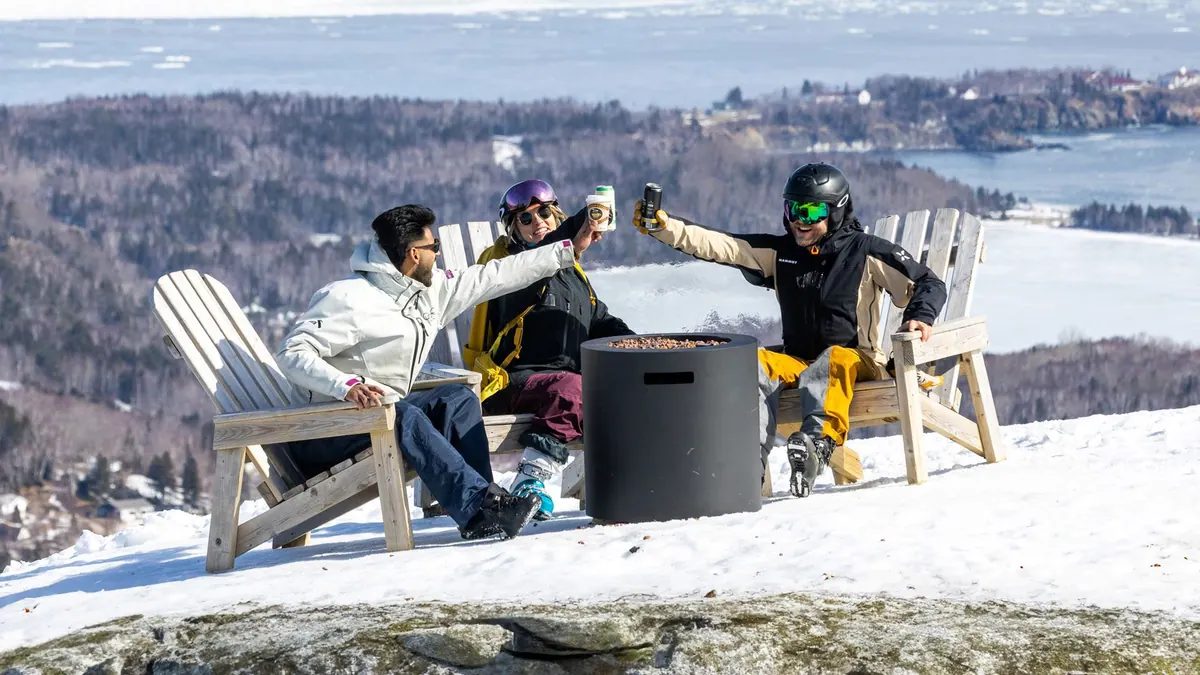 Friends raising drinks in Adirondack chairs on a snowy terrace above the bay