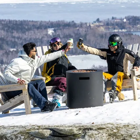 Friends raising drinks in Adirondack chairs on a snowy terrace above the bay