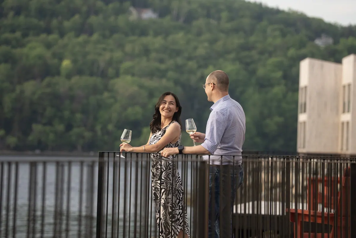 Couple with glasses of white wine on a chalet balcony above the water