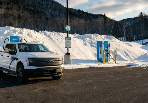 Electric pickup truck plugged into a fast charger in a snowy parking area at Cape Smokey