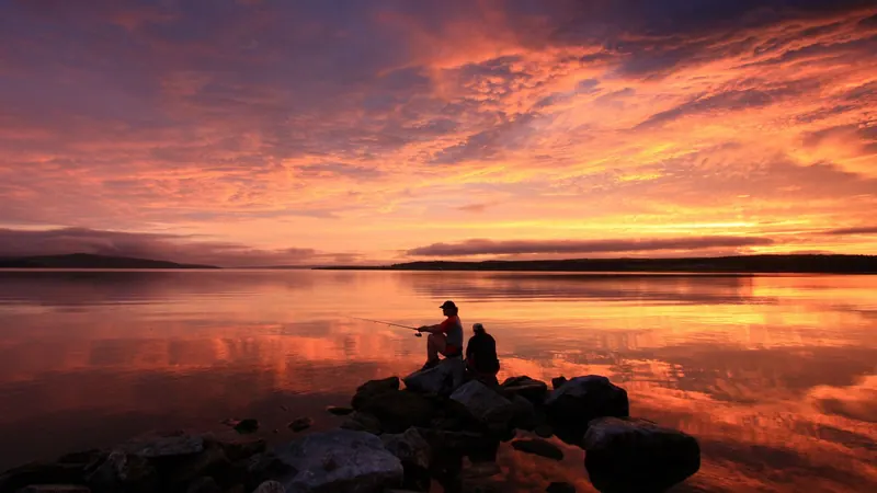 Two people fishing from rocks under a fiery sunset