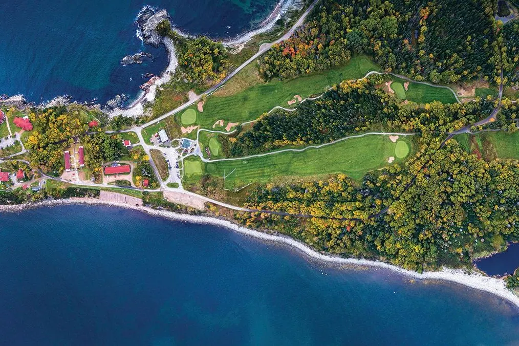 Aerial view of a seaside golf course and lodge on a forested headland above the Atlantic