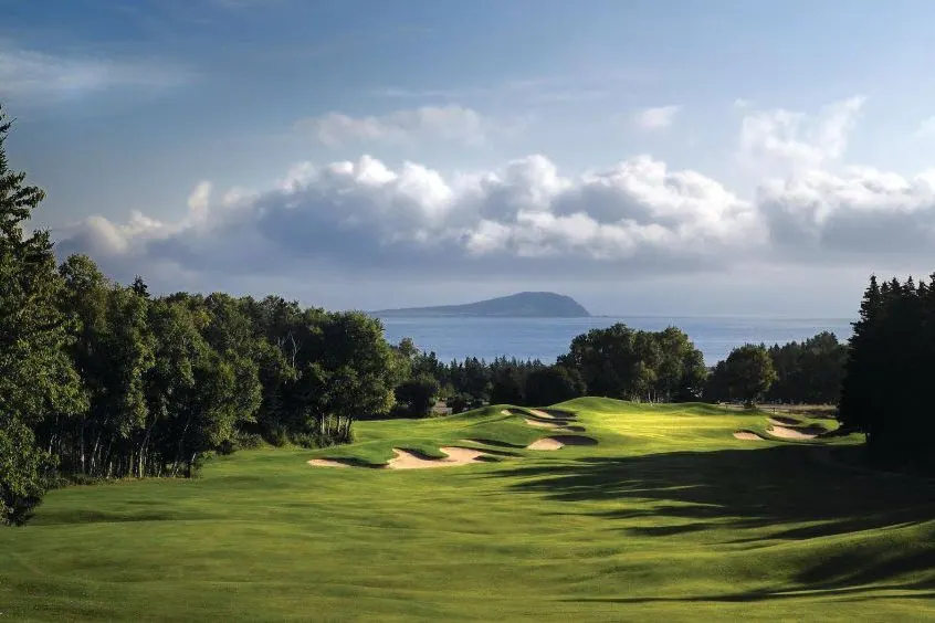 Golf green with bunkers and evergreens overlooking the sea and an island on the horizon