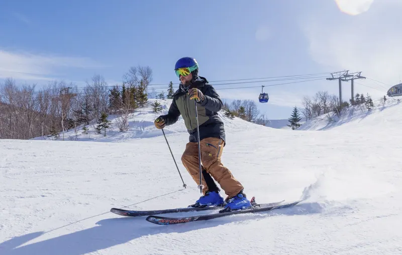 Skier carving a groomed run at Cape Smokey with the gondola behind