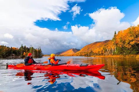 Red kayak on a blue bay below autumn hills