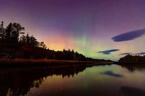Northern lights glowing over a calm lake at dusk